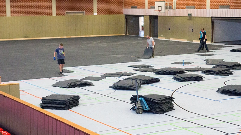 An event floor is laid in a large sports hall. This consists of rubber granulate mats in an interlocking paving design. The event floor protects the hall's sensitive sports floor from damage.
