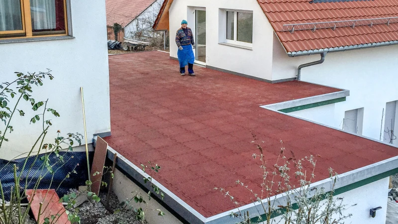 An extension with a flat roof is located between two detached houses. Its flat roof is designed as a terrace and thus made usable for the residents of the neighbouring houses. The roof terrace is made of red WARCO terrace tiles.